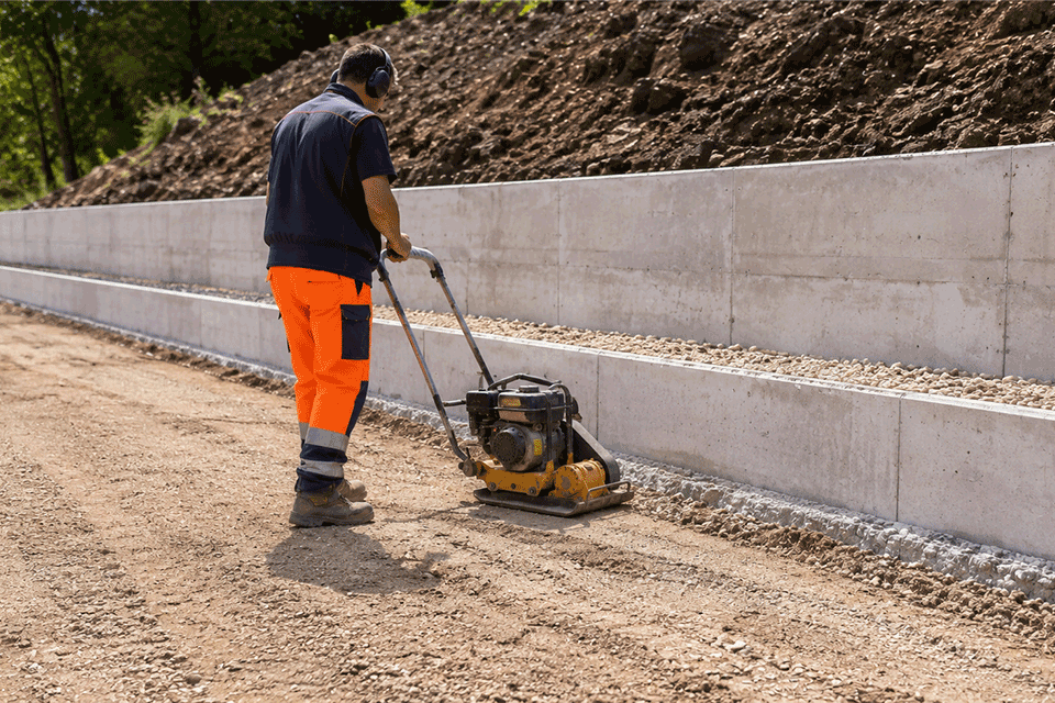 Operatore che compatta il terreno dietro un muro di contenimento con piastra vibrante