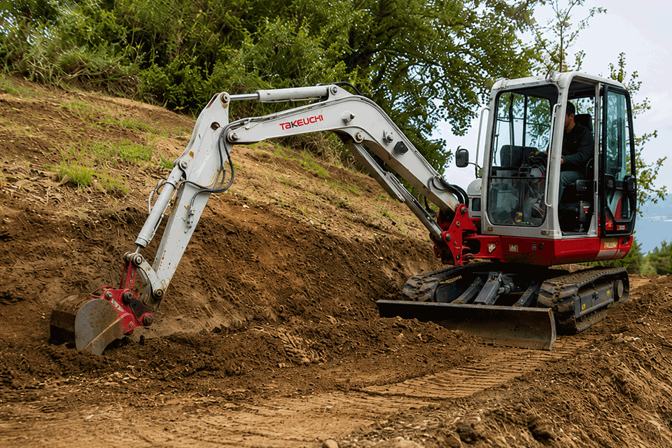 Miniescavatore che prepara lo scavo di base per un muro di contenimento su terreno in pendenza